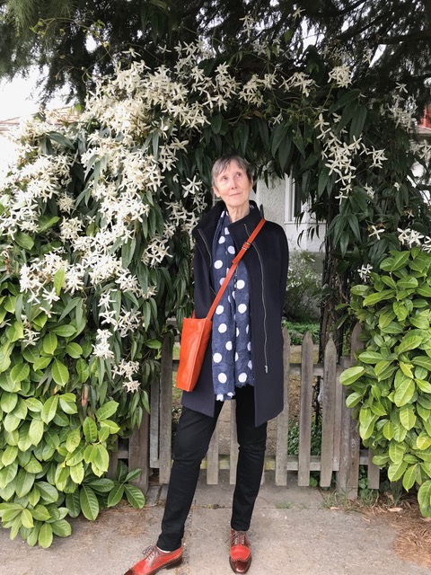 Woman with red handbag and shoes stands in front of a rose arbour